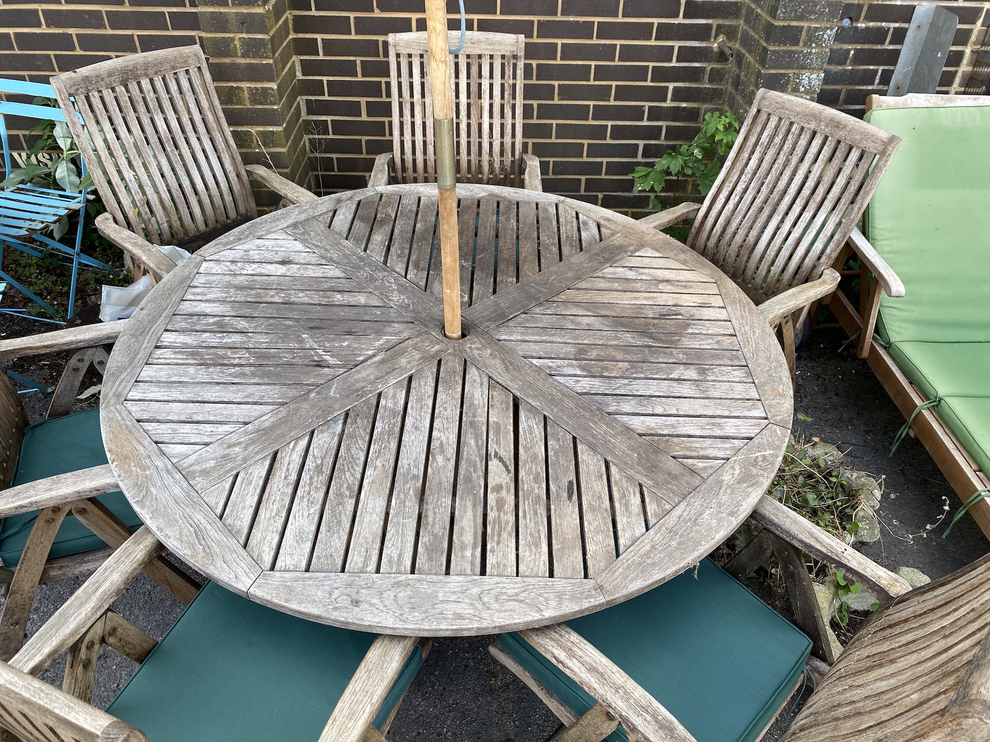 A weathered teak circular garden table, diameter 153cm, height 74cm together with six folding elbow chairs with cushions, stamped 'Regency' and a parasol